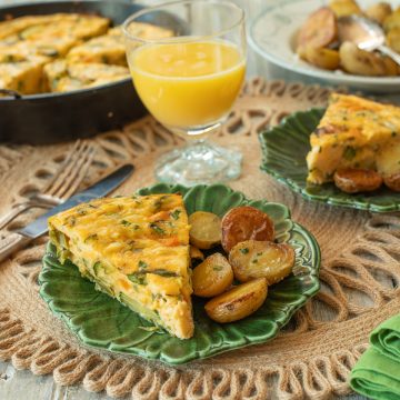 A green plate with a slice of frittata primavera and roasted potatoes.