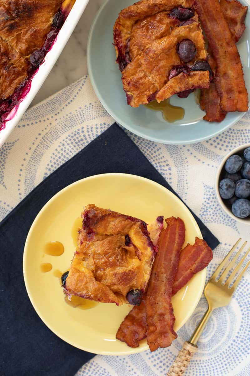 Slice of croissant bake on a yellow plate with a side of bacon.