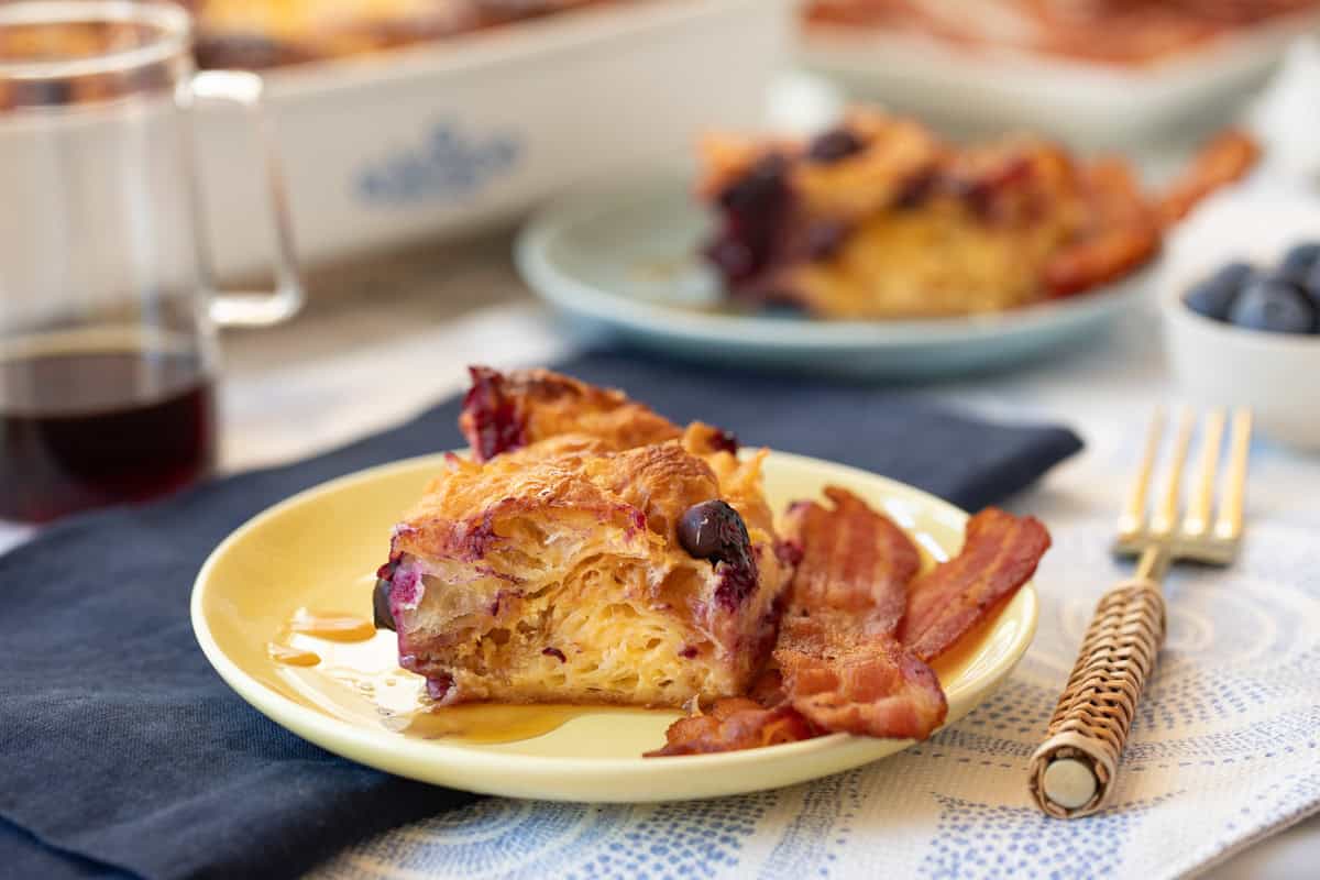 A yellow plate with a slice of a croissant bake with 2 slices of bacon.