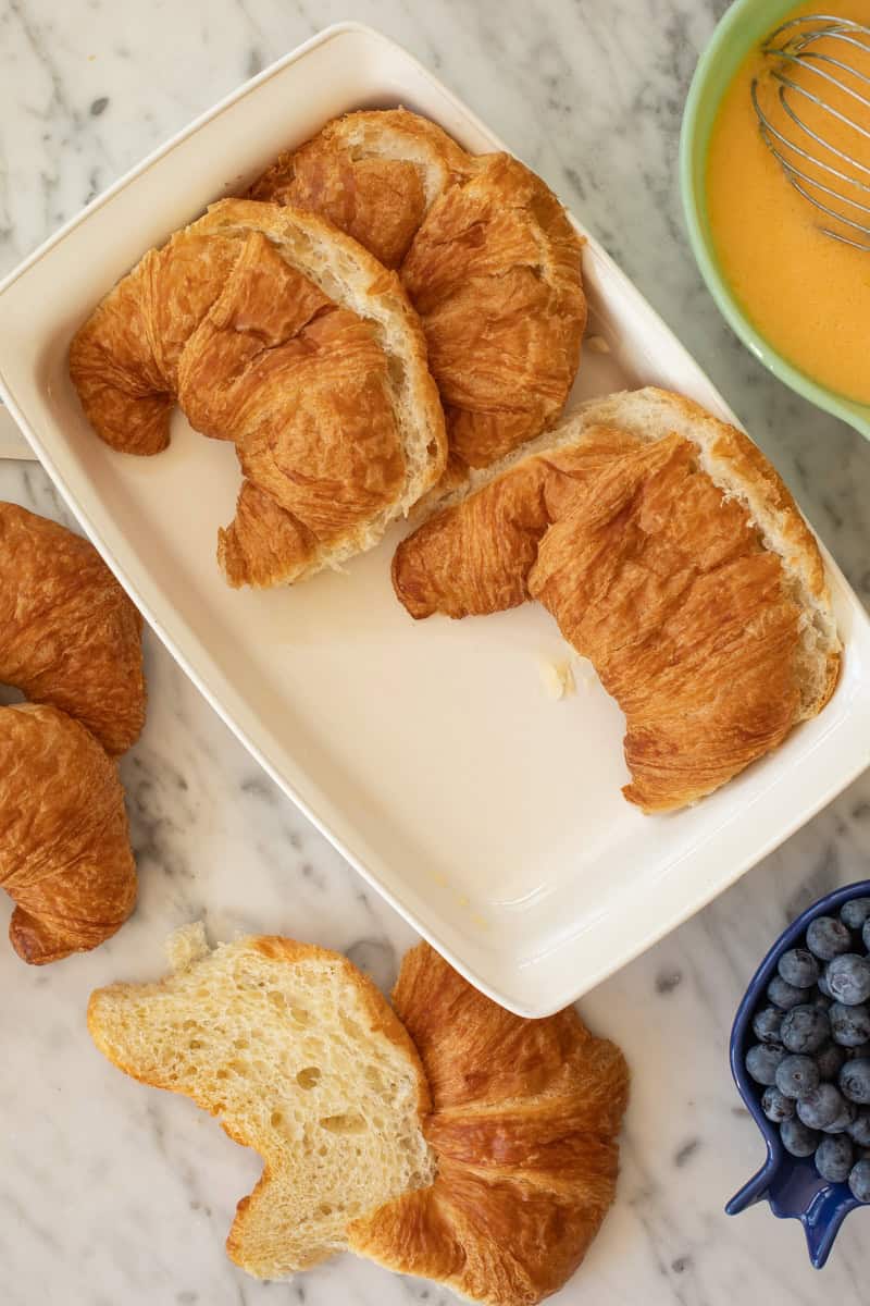 Sliced croissants are layered in a baking dish.