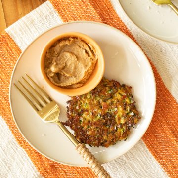 A white plate with a Crispy Pan-Fried Zucchini Fritter and a side dish of Creamy Roasted Walnut Dip.