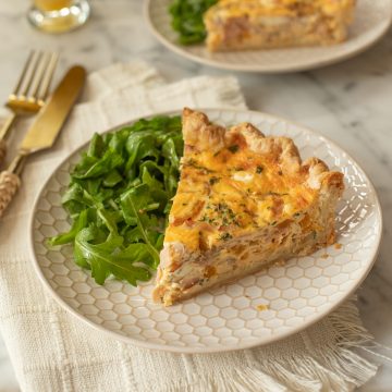 A slice of quiche on a white plate with a side arugula saled.